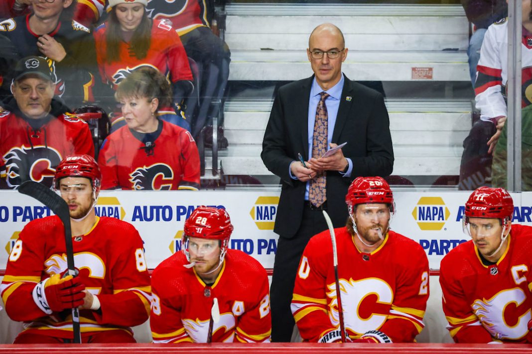 L'entraîneur des Flames de Calgary se tient derrière ses patineurs sur le banc.