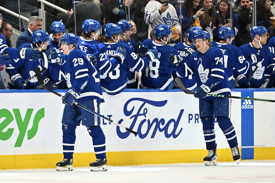 Deux patineurs des Les Maple Leafs de Toronto félicitent leurs coéquipiers sur le banc.
