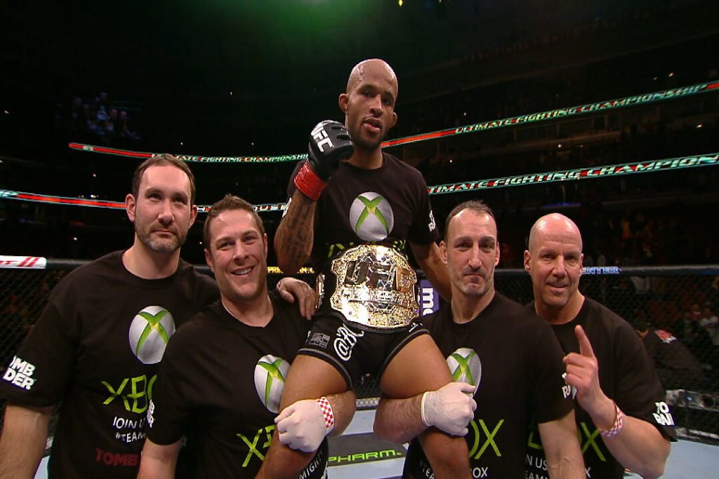 Deux hommes soulèvent le meilleur combattant UFC de l'histoire des poids mouches, Demetrious Johnson.